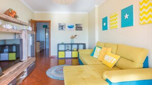 A living room with a yellow sofa, wooden shelves, a TV, and artwork on the wall. - Albufeira Terrace Pool Garage Dream Flat (Albufeira)