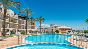 A swimming pool with a curved design, surrounded by a metal fence. There are palm trees and lounge chairs visible. - Albufeira Terrace Pool Garage Dream Flat (Albufeira)