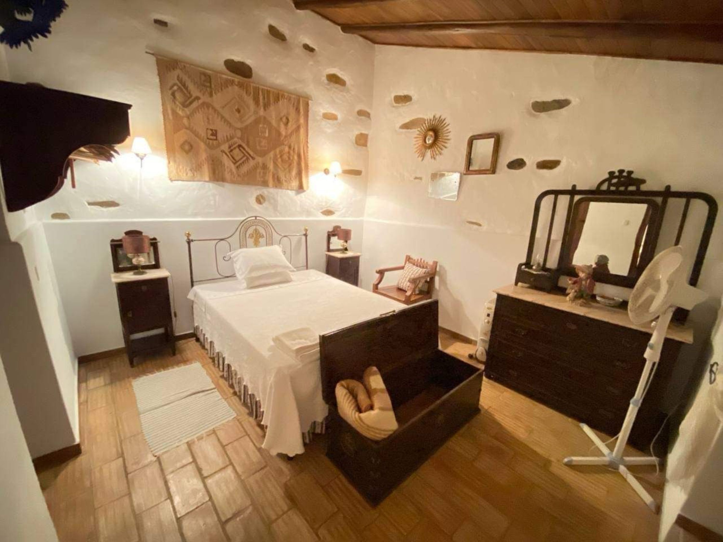 Een slaapkamer met een bed, nachtkastjes, een kaptafel, een spiegel en een houten stoel.