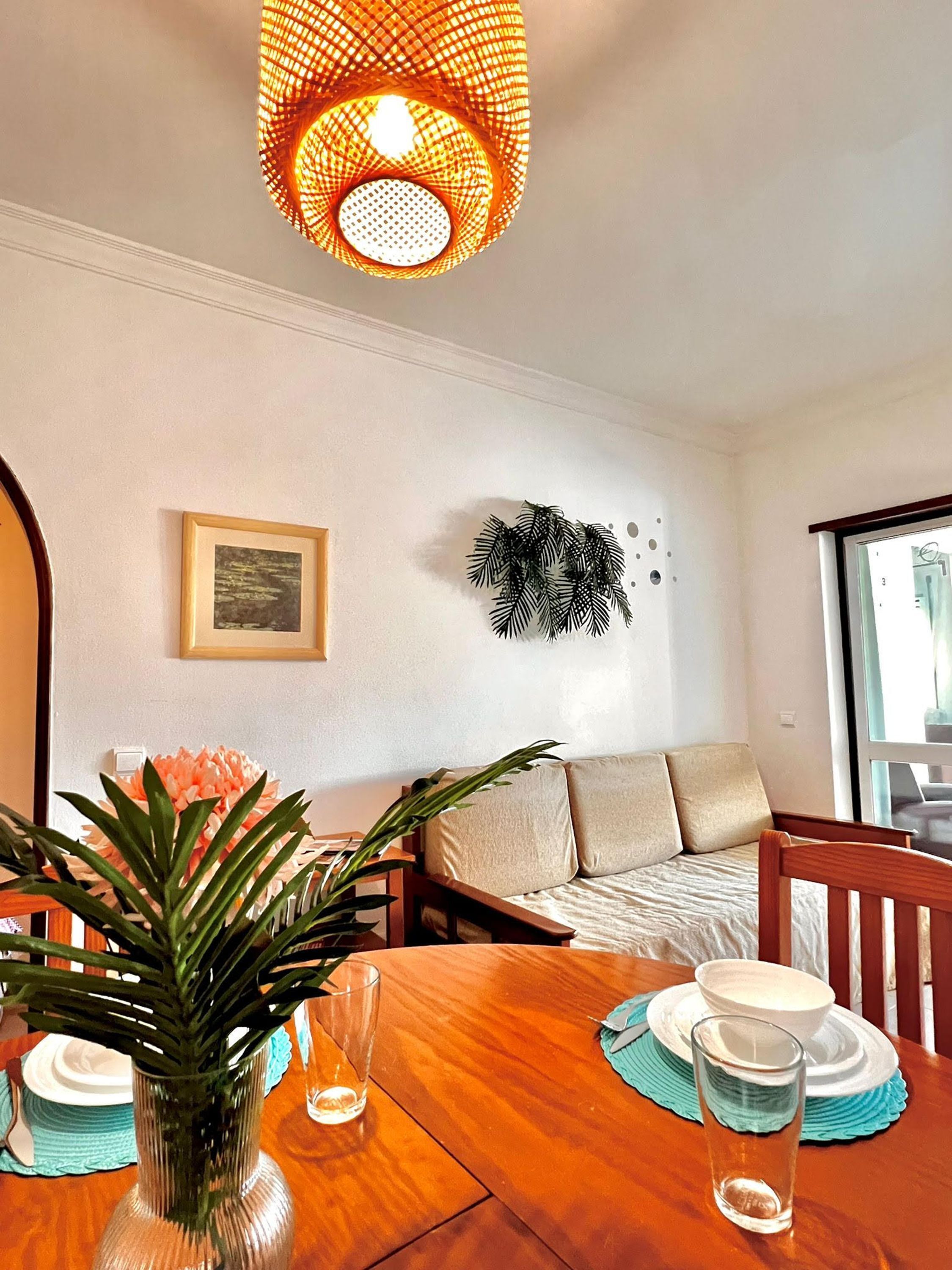Un comedor con una mesa de madera, un florero con planta y una lámpara de pared.