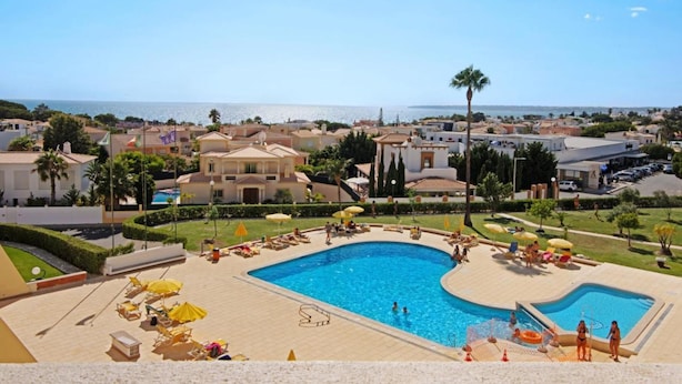 A resort with a large swimming pool surrounded by sun loungers and umbrellas, a clear view of the sea, and a Mediterranean-style architecture. - Ground Floor Palmeira Gal Villa With Pool (Albufeira)