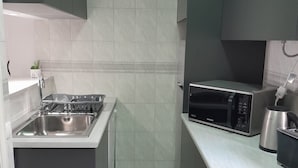 A compact kitchen with a built-in sink, a microwave, and a kettle on the countertop. - Ground Floor Palmeira Gal Villa With Pool (Albufeira)