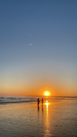 A beach scene with two people standing near the water during sunset.