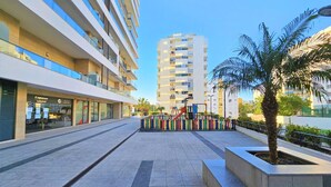 A modern urban plaza with a playground, a palm tree, and multi-story buildings in the background. - Superior Garage Balcony Praia da Rocha Prime Flat (Portimão)
