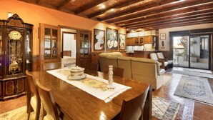 A dining area with a wooden table, chairs, and a clock. There is a sofa and a kitchen in the background. - Private Pool Villa 20min by Porto (Oliveira De Azemeis)