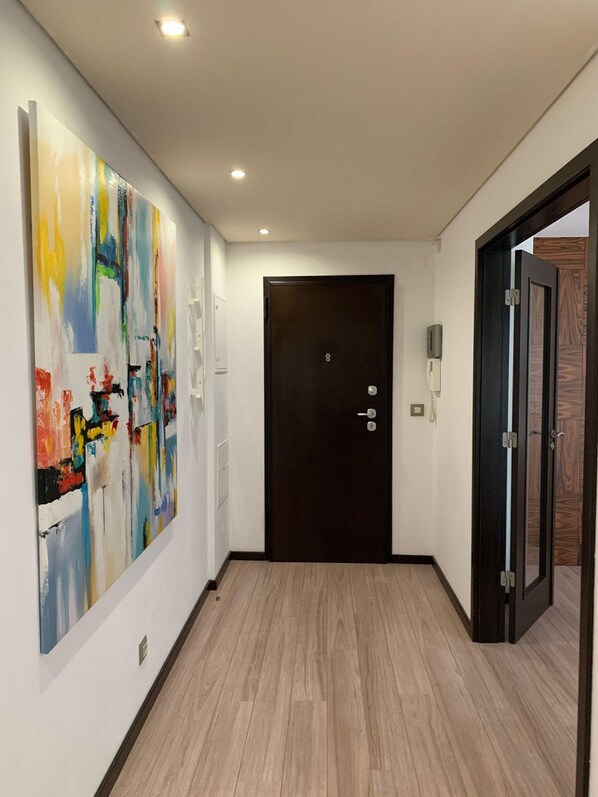 A hallway with a wooden floor, a dark door, and a colorful abstract painting on the wall. - Modern Flat Near Lisbon (Seixal)