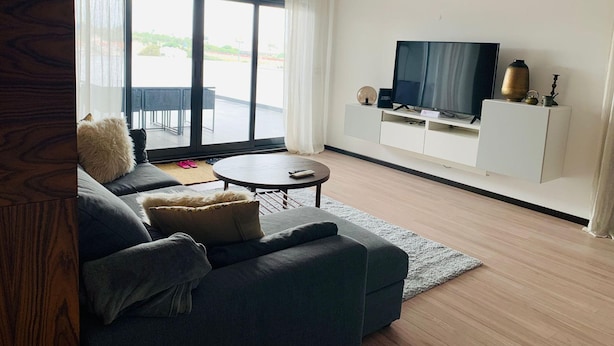 Un soggiorno moderno con un divano grigio, un tavolino rotondo e una TV su un mobile bianco.