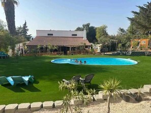 A swimming pool surrounded by a well-maintained lawn, with a building featuring a tiled roof in the background. - Porches Private Pool Villa 17 Guests (Lagoa)
