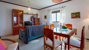 Een gezellige woonkamer met een bank, televisie, houten kasten en een eettafel met stoelen.