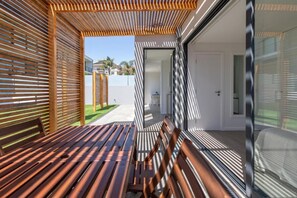 A modern outdoor seating area with wooden slatted benches and a glass door leading to a white interior space. - Another Side in Ovar (Ovar)