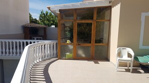 A balcony with a white balustrade, a glass door with a metal handle, and a white plastic chair.