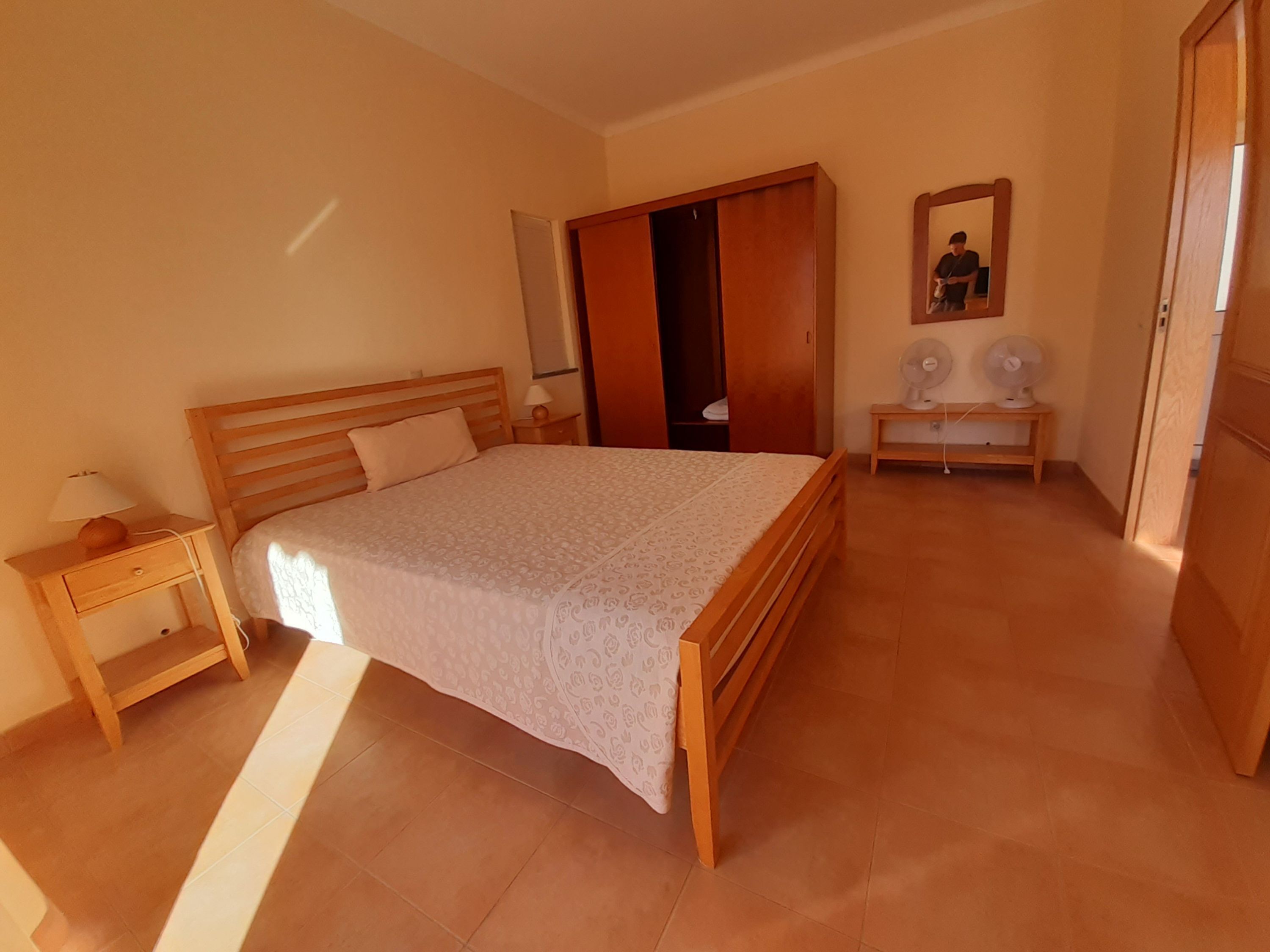 Ein Schlafzimmer mit einem Holzbett, einem Nachttisch, einem Kleiderschrank und einem Spiegel.