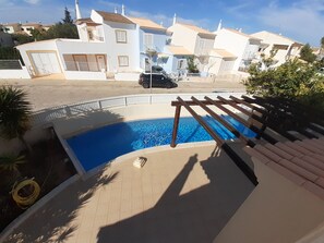 A residential area with a swimming pool, a car parked on the street, and houses with balconies.