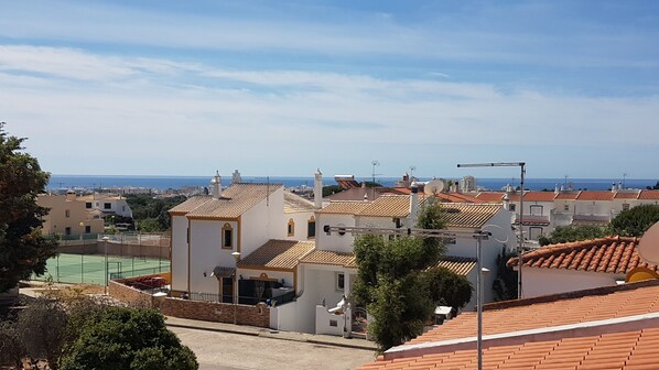 A coastal residential area with terracotta-tiled roofs, white buildings, and a tennis court.