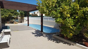 Una piscina con solárium de baldosas, una pérgola y plantas en macetas.