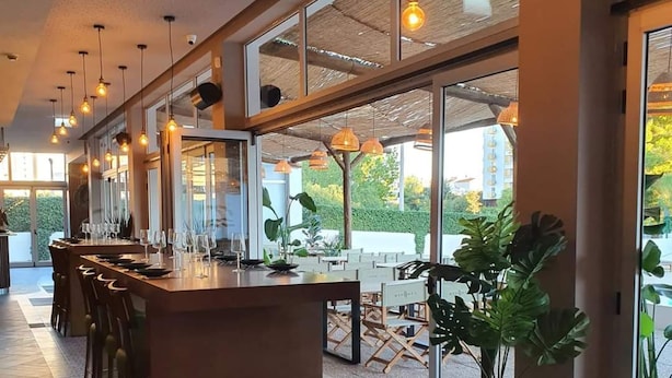 A modern restaurant with a long counter, wicker chairs, and large windows offering a view of the outdoors. - Green Tower Sea View With Garage and Balcony (Portimão)