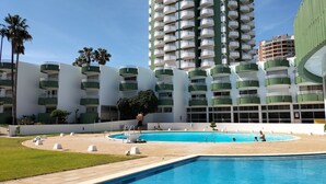 A hotel with a pool area, multiple floors, and a tall building in the background. - Green Tower Sea View With Garage and Balcony (Portimão)