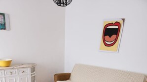Una sala de estar con un sofá, una mesa de centro de vidrio, un tapete amarillo y un mueble blanco.