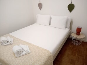 Een net opgemaakt bed met witte lakens en twee opgerolde handdoeken op een bed met een patroon.