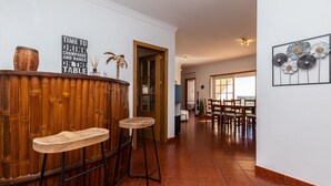 A bar area with wooden stools, a sign reading "TIME TO DRINK CHAMPAGNE AND DANCE ON THE TABLE", and a dining area with wooden chairs and a table. - Beach Front View Armacao de Pera Flat (Silves)