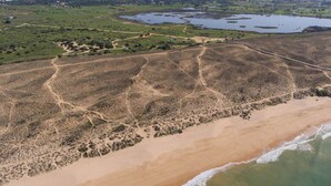 An aerial view of a coastal area with a sandy beach, a winding road, and a large body of water. - Beach Front View Armacao de Pera Flat (Silves)