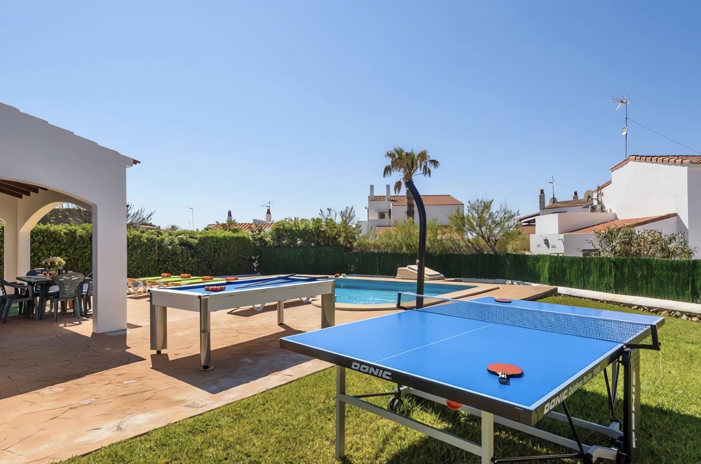 An outdoor pool area with a ping pong table, a pool table, and a seating area with chairs and a table.