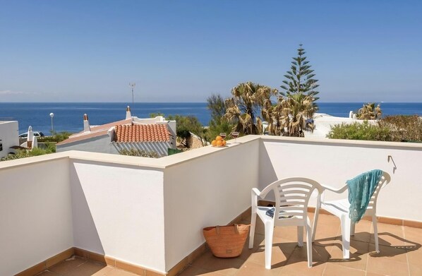 A rooftop terrace with a view of the sea, white chairs, and a basket.