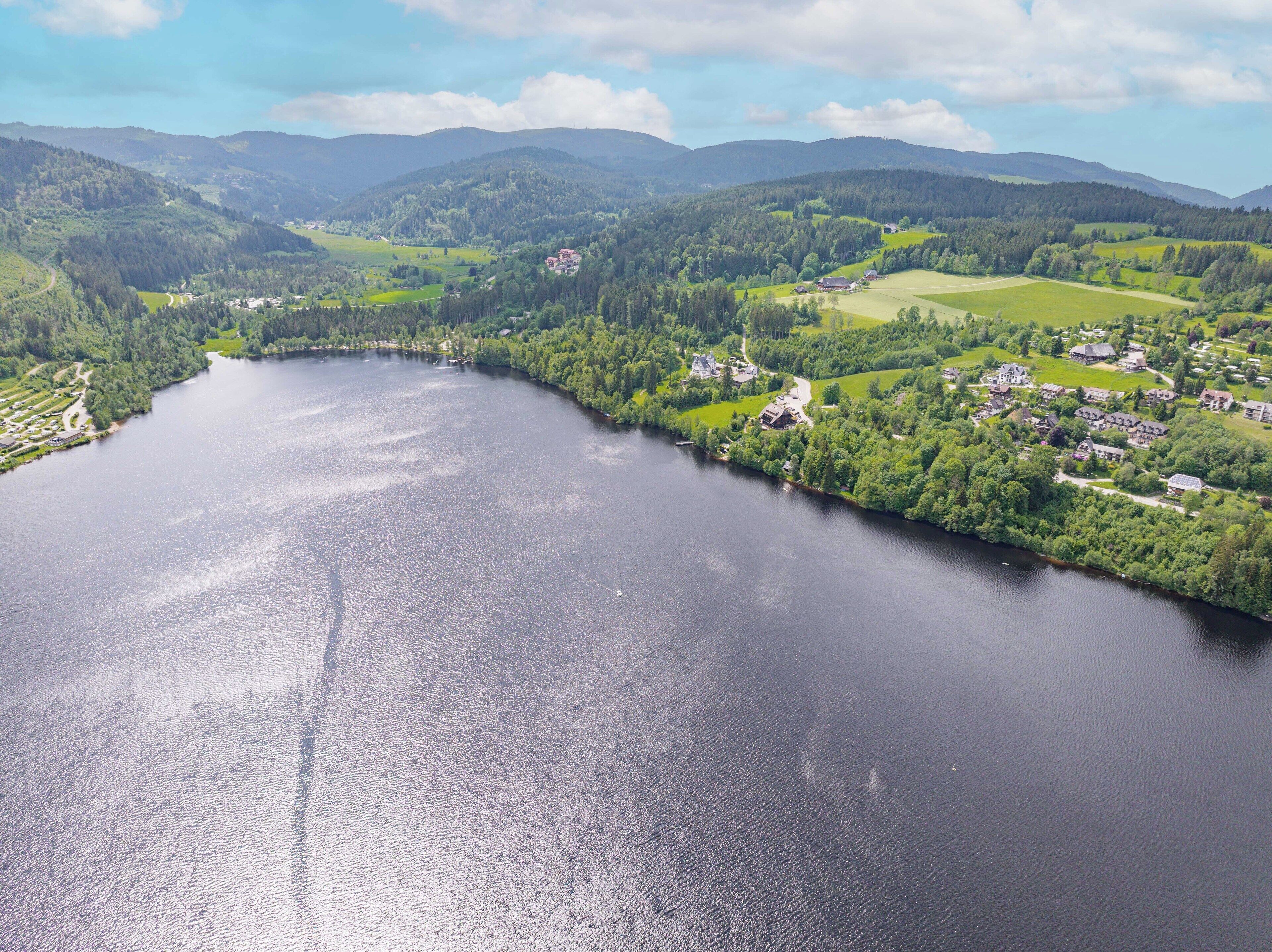 Ein Anwesen am See mit Seeblick, umgeben von bewaldeten Hügeln und einem kleinen Dorf.