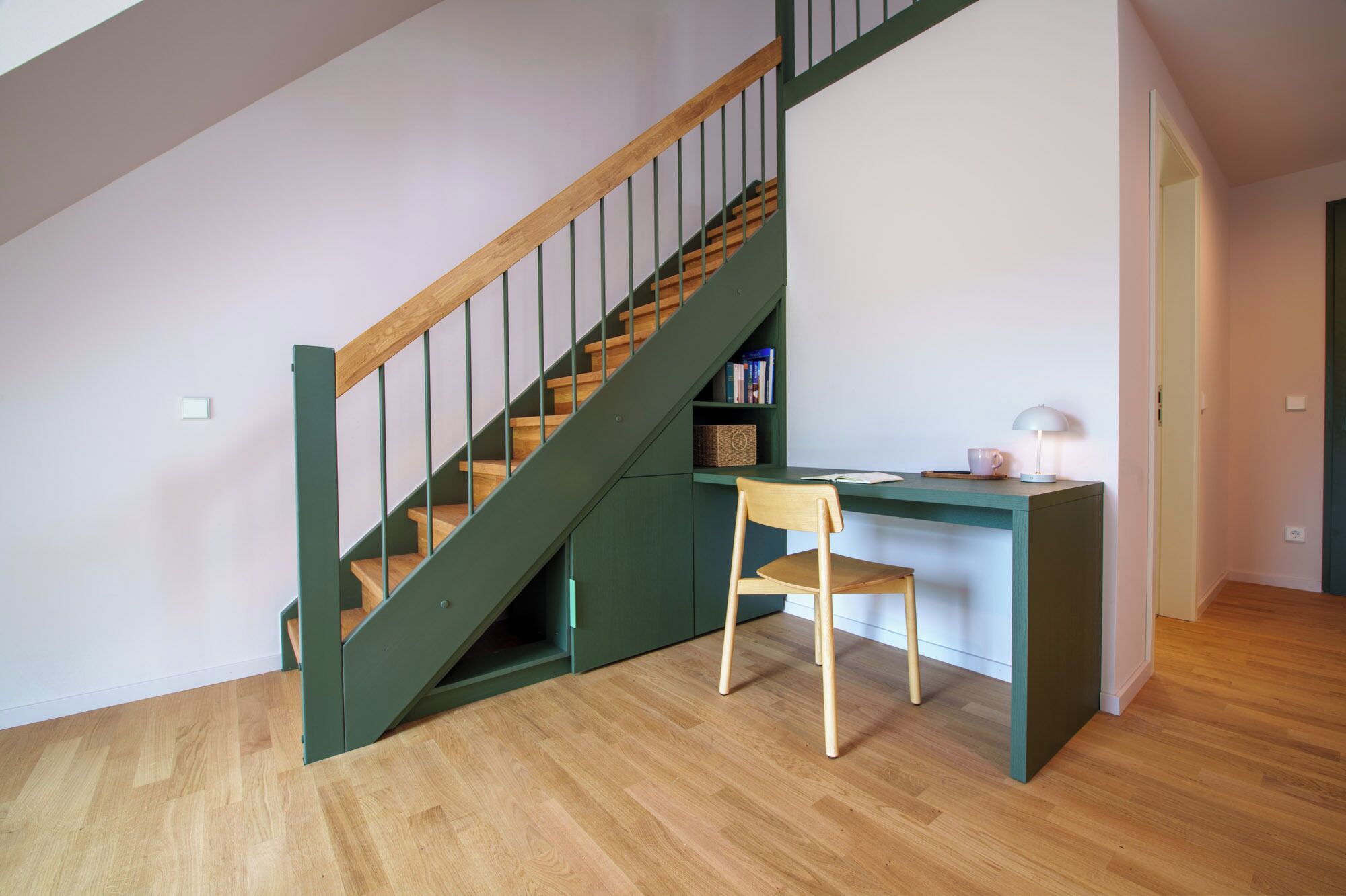 Eine Treppe mit Holzboden und grünen Geländern, ein Schreibtisch mit Stuhl und eine Lampe.
