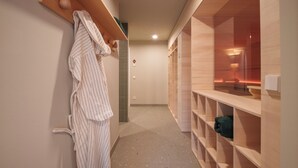 A hallway with a wooden bench, a robe hanging on the wall, and a sauna area with a glass enclosure. - stuub titisee (Titisee-Neustadt)