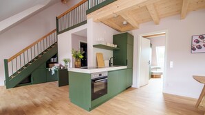 A modern kitchen with a green island, wooden staircase, and a view into another room. - stuub titisee (Titisee-Neustadt)