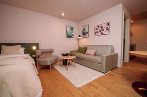 Un dormitorio moderno con cama, sofá, sillón, una mesita y obras de arte en las paredes.