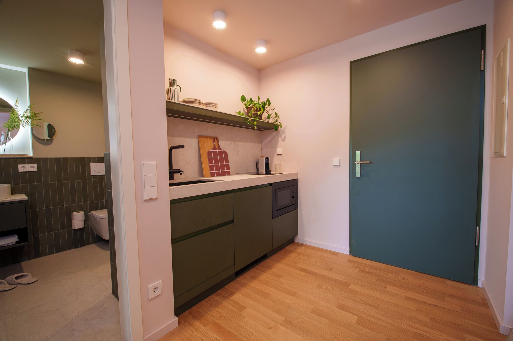 A compact kitchen with a built-in dishwasher, a sink, and a countertop. There is a door to the right and a mirror on the left.