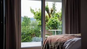 A bedroom with a large sliding glass door leading to a balcony with a view of greenery and a chair. - stuub titisee (Titisee-Neustadt)