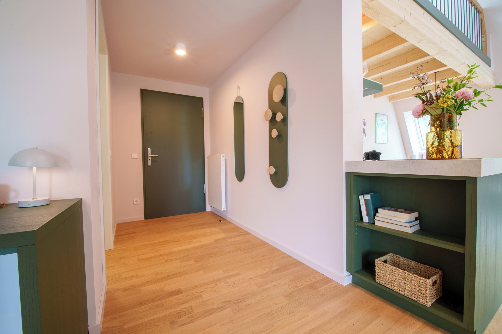 Een gang met houten vloer, een groene deur en een plank met boeken en een mand.