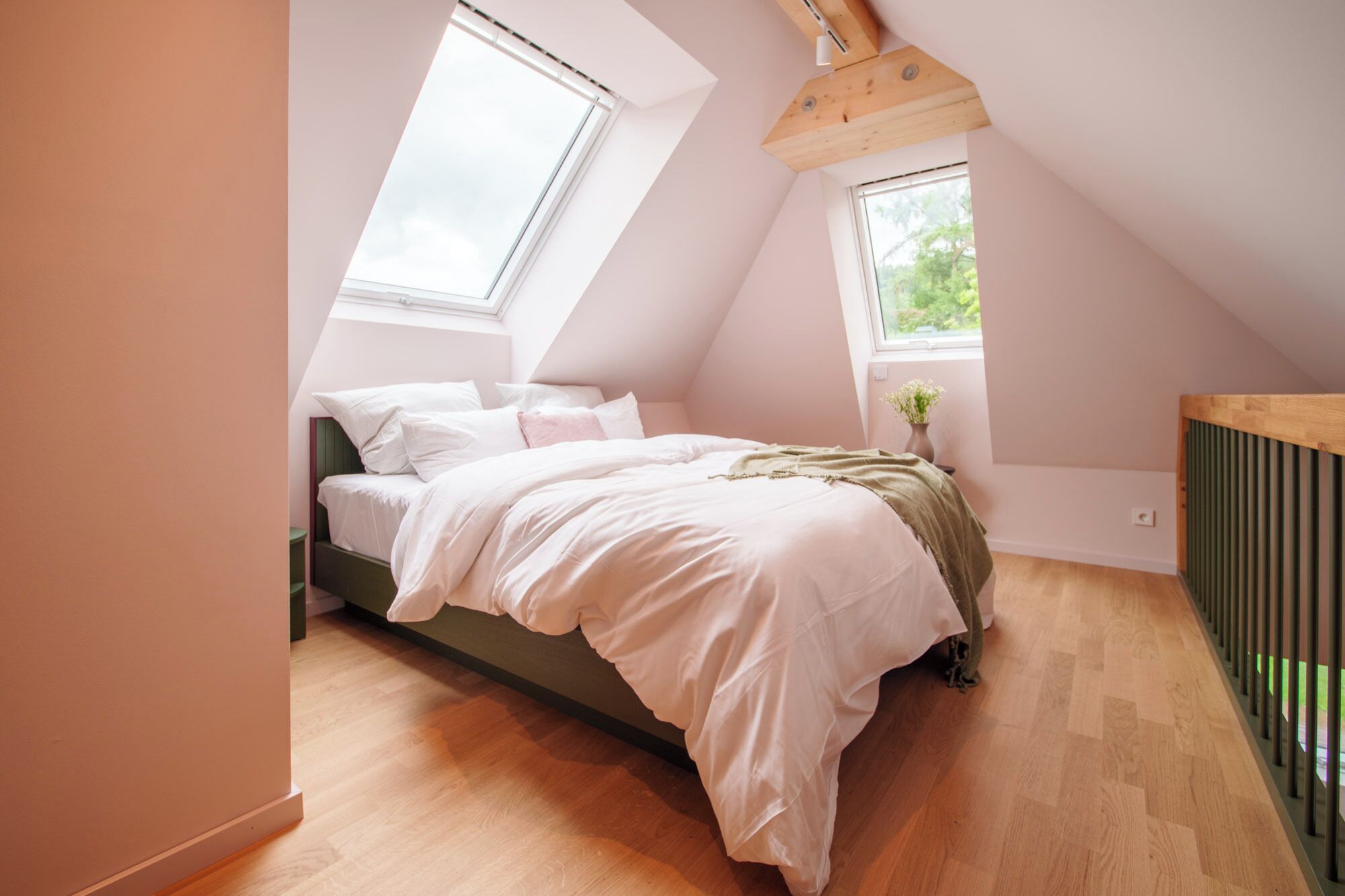 Ein Schlafzimmer mit schrägverdeckter Decke, einem Bett mit weißer Bettwäsche, einem kleinen Fenster mit einer Pflanze und einem Heizkörper.
