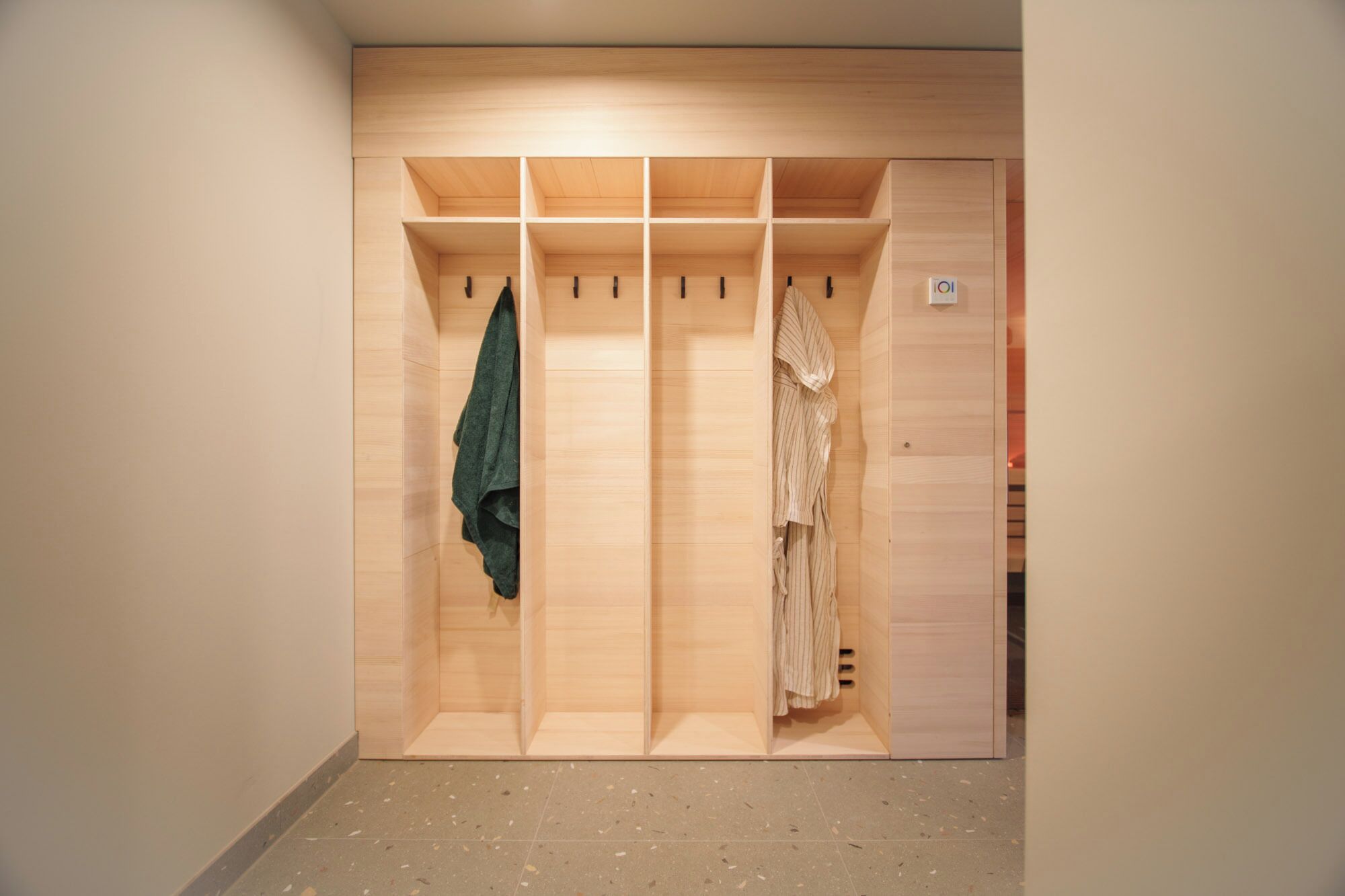 Un dressing accessible sans porte, doté de nombreuses étagères et d’espaces pour suspendre les vêtements, avec une finition en bois clair et un sol carrelé.