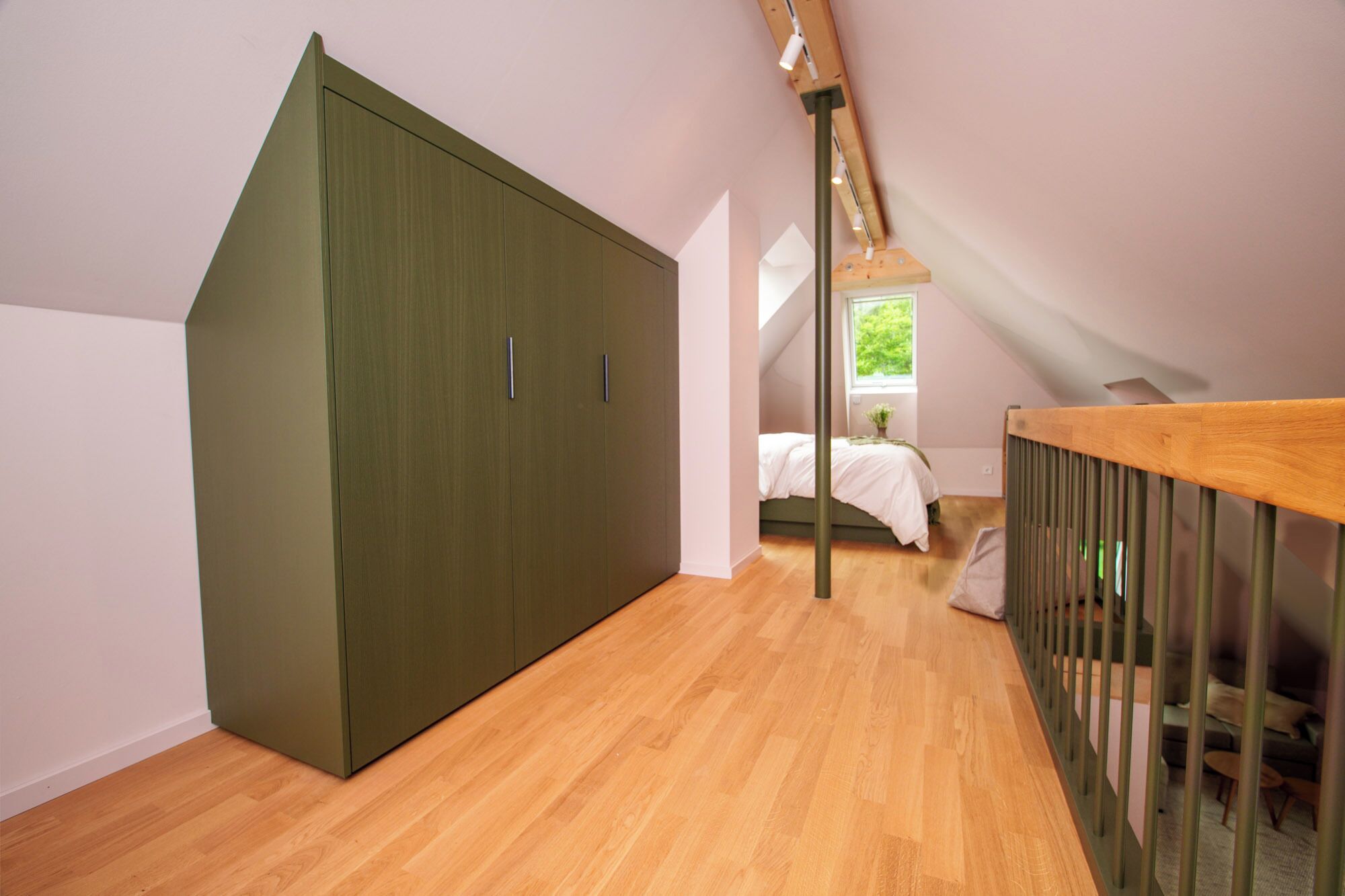 Une chambre avec un plafond en pente, un plancher en bois, une armoire verte et un lit avec une tête de lit blanche.