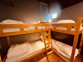 A bunk bed room with a ladder, wooden floors, and a window with natural light.