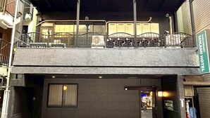 A multi-story building with a green and yellow facade, a covered outdoor seating area on the ground floor, and a visible entrance to a business on the right. - Mikami Asakusabashi Hotel (Tokyo)