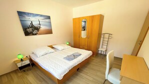 Un dormitorio con cama, lámparas de noche, escritorio, silla, armario y un cuadro en la pared.