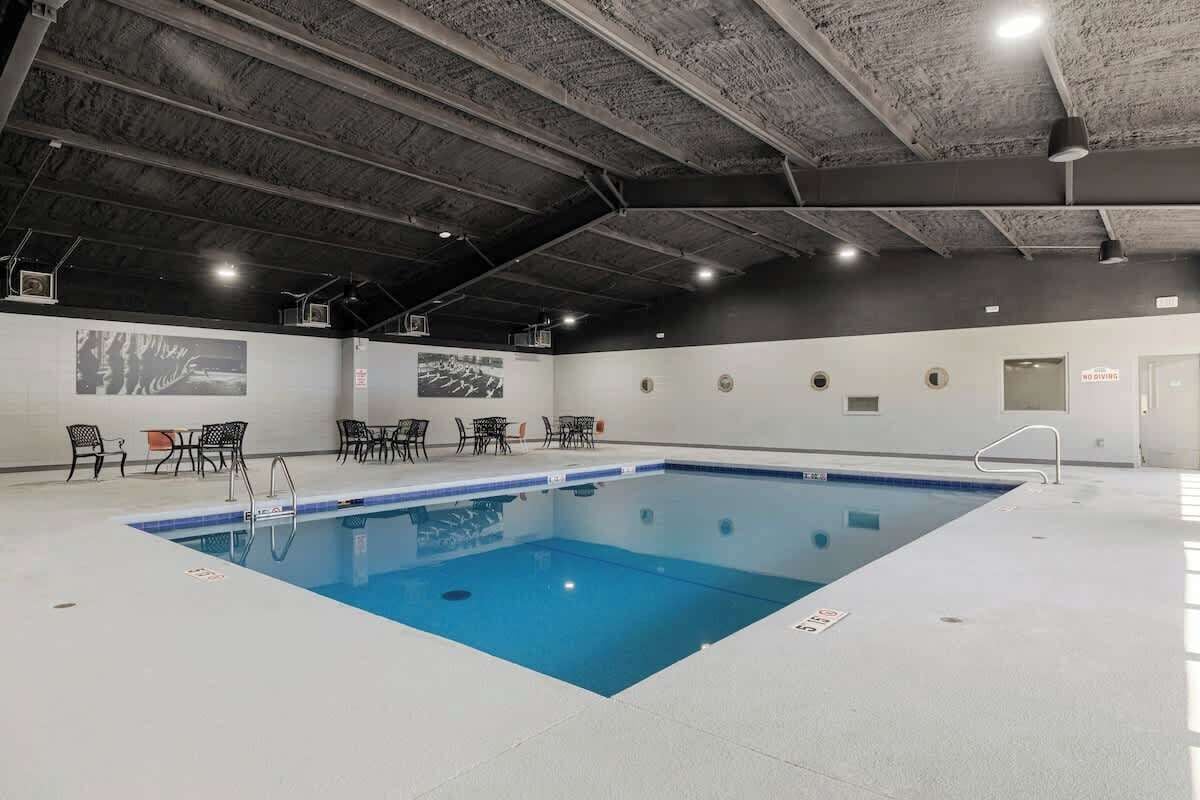 An indoor swimming pool with a blue water feature, surrounded by black chairs and tables, and a ceiling with exposed beams.