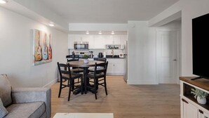 Eine moderne Küche mit weißen Schränken, ein Essbereich mit Holztisch und -stühlen sowie ein Flachbildfernseher auf einem Holzständer.