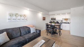 A modern living room with a grey sofa, a wooden coffee table, and a dining area with a table and chairs. A kitchen is visible in the background with white cabinets and a stainless steel oven. - 109 Ground level, Walk to Convention Center and Landing (Branson)