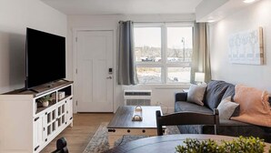A living room with a flat-screen TV on a wooden stand, a white cabinet with glass doors, a gray sofa with cushions, a coffee table, and a window with curtains. - 109 Ground level, Walk to Convention Center and Landing (Branson)