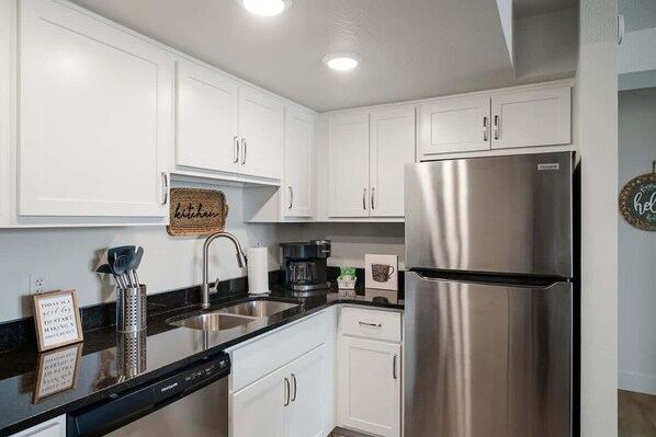 A modern kitchen with white cabinets, stainless steel appliances, and a black countertop.