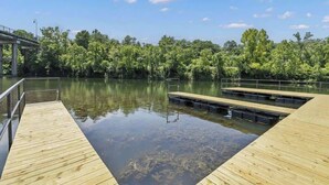 Une jetée en bois s’étendant sur un lac paisible, entourée d’une végétation luxuriante et sous un ciel bleu clair.