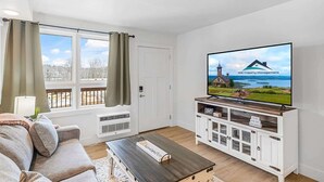 A living room with a large flat-screen TV, a sofa, a coffee table, and a window with curtains. - 203 Walk to The Landing & Convention Center (Branson)