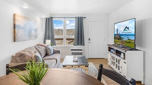A modern living room with a sofa, coffee table, TV, and a view of a scenic landscape through the window. - 203 Walk to The Landing & Convention Center (Branson)
