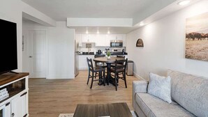 A modern living room with a grey sofa, a coffee table, and a TV on a wooden stand. A dining area with a round table and chairs is visible in the background. - 203 Walk to The Landing & Convention Center (Branson)